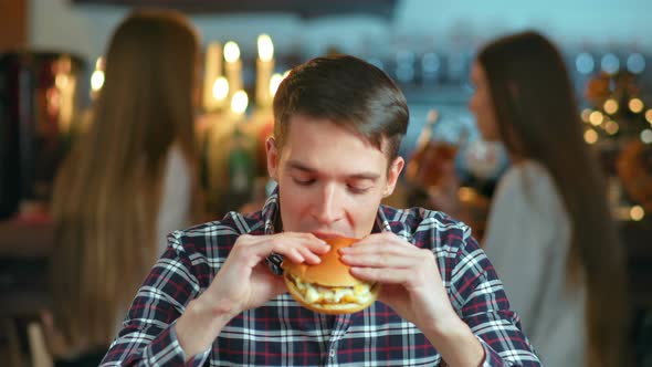 Man in a Restaurant Eating a Hamburger and Smiling