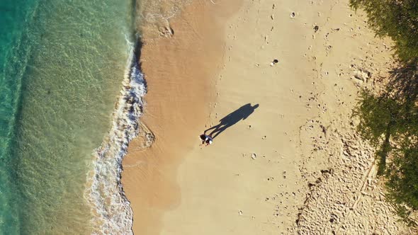 Hugging couple walking slowly on quiet exotic beach washed gently by ocean waves at early morning in