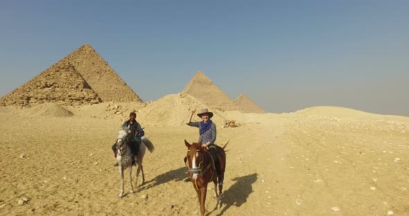 Happy woman riding horse with local man in front of Giza pyramids