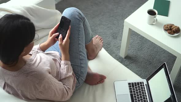 Woman Sits on Couch Near Table and Presses Phone Button Spbd