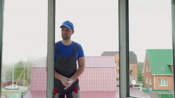 Handyman in Uniform Cleans Windows in Cottage Outdoors