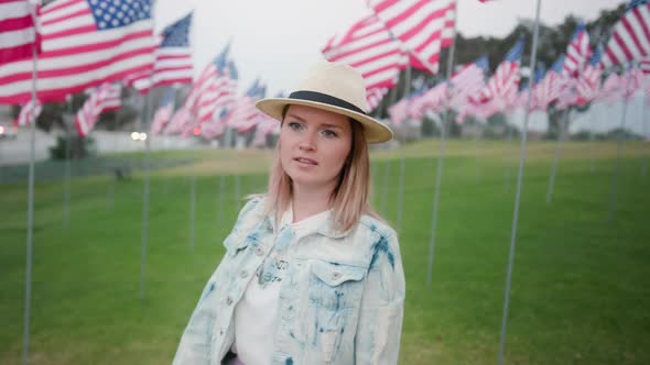 Portrait of Calm Young Woman Walking in Green Park Between Waving American Flags