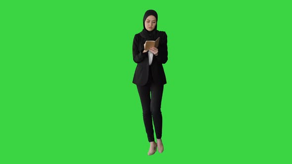 Muslim Businesswoman Thinking and Writing Ideas in Her Notepad While Walking on a Green Screen