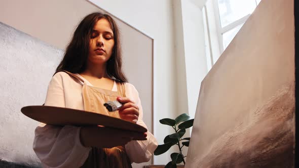 Art Studio  Young Woman Applying Painting Varnish on the Canvas