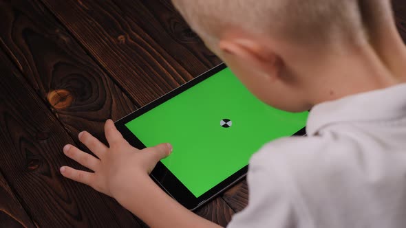 Closeup of a Child Holding a Tablet with a Green Screen on a Wooden Background