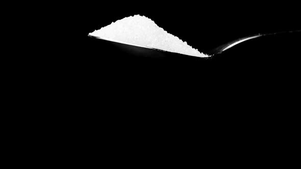 White Cane Sugar Falling Down From Teaspoon Isolated on Black Slow Motion