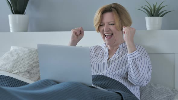 Reaction of Success by Happy Senior Woman Using Laptop in Bed