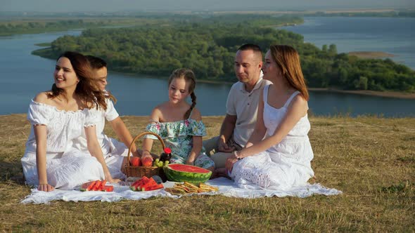 Happy Family with Children Has Picnic on Hilly Riverbank