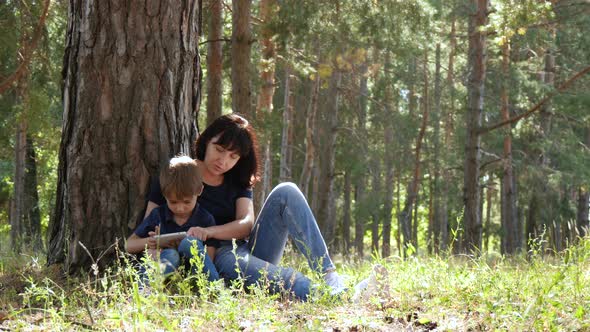 Happy Family: Mother and Son Relax Sitting in the Park By a Tree. A Woman and a Child Look