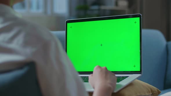 Close Up Of A Man Waving Hand And Talking To Green Screen Laptop While Lying On Sofa