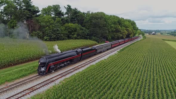 An Aerial Front to Side View of a Steam Passenger Train Blowing Smoke at a Small Station Waiting For