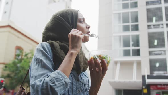 Woman wearing hijab eating a takeaway salad in the street