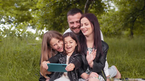 Cheerful Parents and Their Cute Daughters Sitting Together on Green Grass and