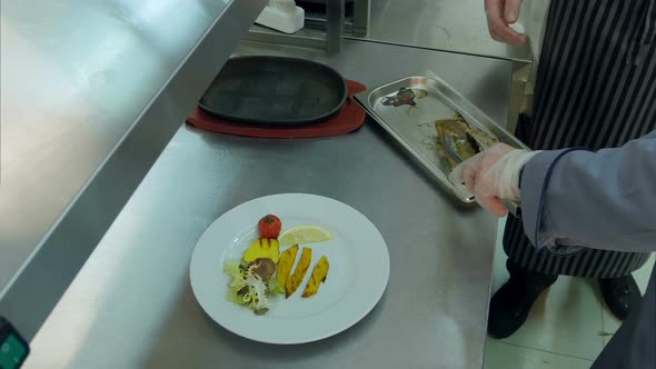 Chef Explaining Cook Trainee How To Put Fish on a Plate with Vegetables