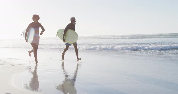 Happy african american couple running with surfboards on sunny beach