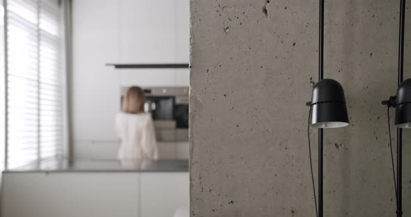 A Woman Makes a Coffee in a Minimalist Interior with Focus on the Lamp