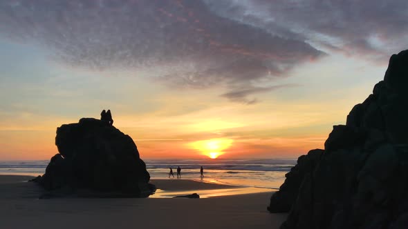 People sitting on rocks and walking on beach at sunset at the Oregon Coast