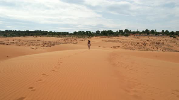 slow low aerial of footsteps in the sand as woman walks top of dunes in desert