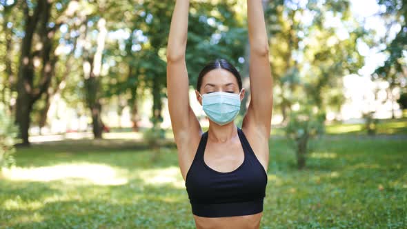 Athletic Young Woman in a Medical Protective Mask Doing Yoga in the Park