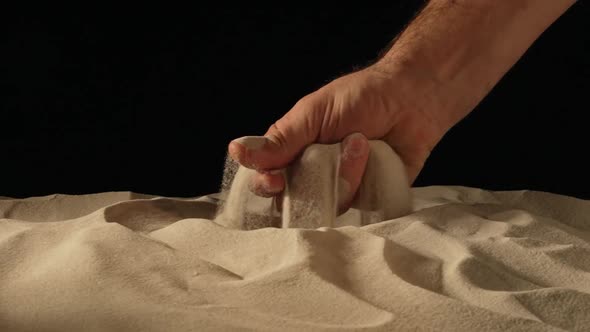 Male Hand Squeezing and Spilling a Handful of Dry Sand on Black Studio Background