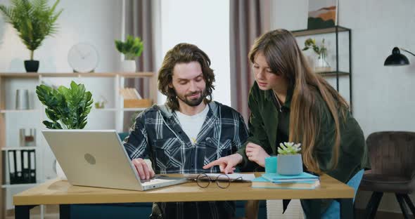 Guy Working on Laptop at Home when Beautiful Positive Female Colleague Approaching to Him