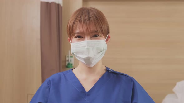 Portrait of Asian female nurse in scrub uniform wearing mask and smile, look at camera in hospital.