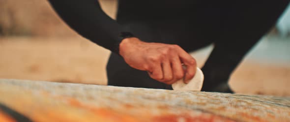 Hand of a man applying wax to a surfboard at the beach