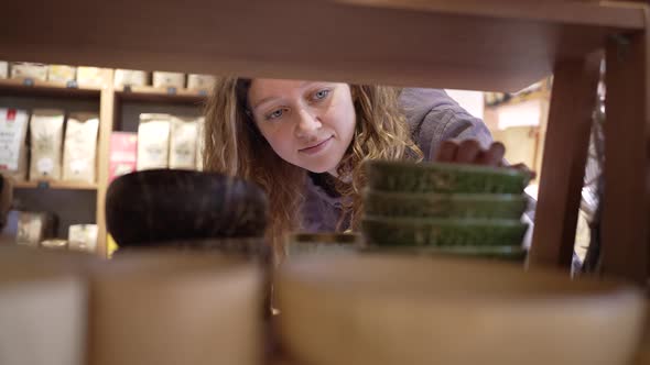 Young Woman Takes Bowls Standing on Shelf in Supermarket