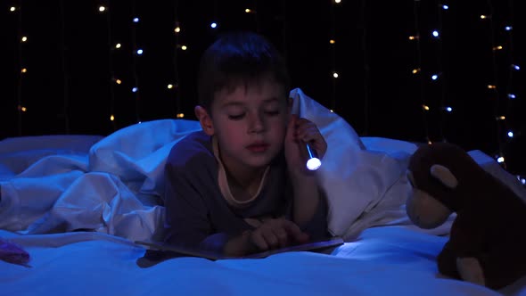 Child at Night Reading a Book on the Bed. Bokeh Background