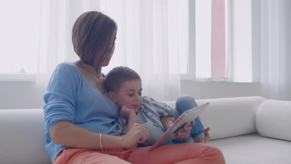 Happy Family Mom and Kid Son Using Digital Tablet Sitting on Sofa Smiling Parent Mother with Child