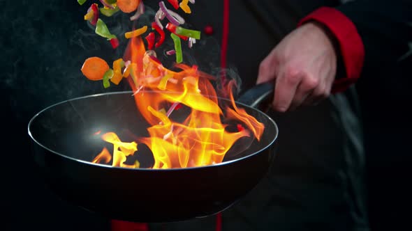 Super Slow Motion Shot of Chef Holding Frying Pan and Falling Vegetables Into Fire at 1000Fps.