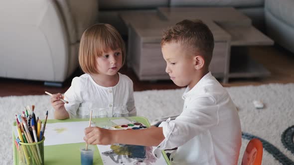 Portrait of Two Kids Holding Paintbrushes and Drawing at Home