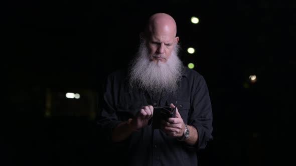 Portrait Of Bald Man With Beard Using Mobile Phone Outdoors At Night