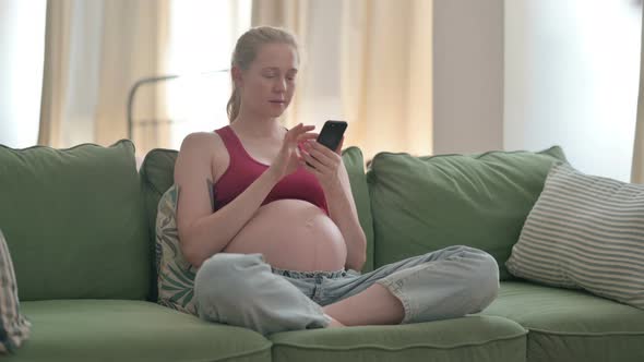 Pregnant Woman Using Smartphone While Sitting on Sofa