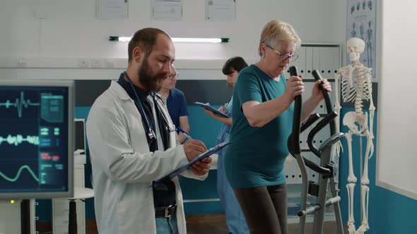 Osteopath Taking Notes and Watching Patient Use Stationary Bicycle