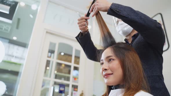 Professional male stylist wearing mask and face shield cutting woman's hair in salon during Covid19