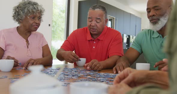 Happy senior diverse people playing puzzle at table at retirement home