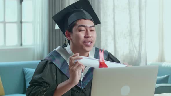 Excited Asian Man Showing Off A University Certificate During An Online Video Call At Home