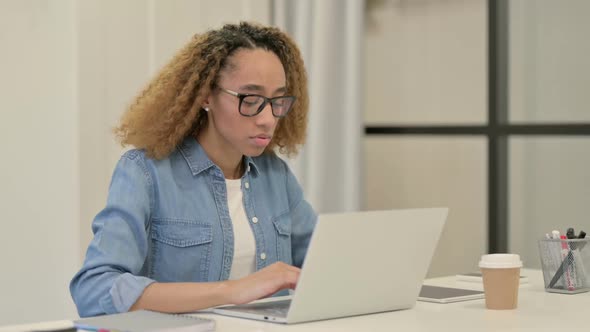 African Woman Smiling at Camera While Working on Laptop