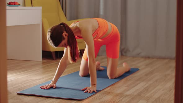 Young Slim Woman in Orange Clothes Working Out with Her Back on Yoga Mat