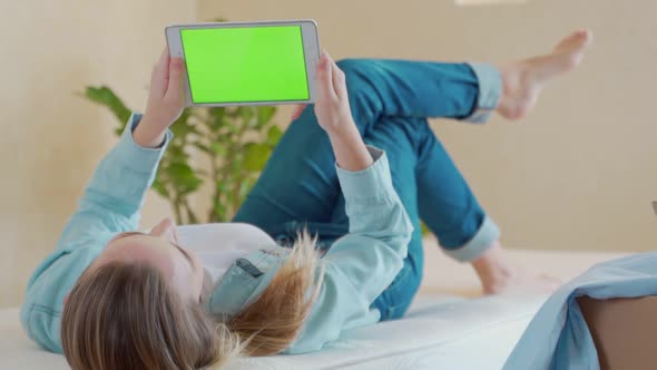 A Woman Lying on a Bed Using a Digital Tablet with a Green Screen
