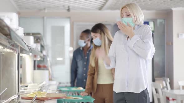 Ill Young Blond Woman in Face Mask Sneezing and Queue Moving Away in Lunchroom