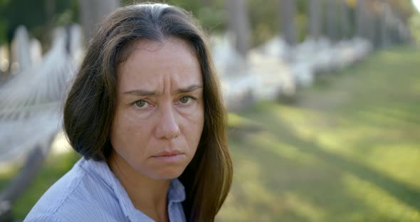 Sad Middle Aged Woman Is Looking at Camera in Garden Area in Summer, Moving Brows and Frowning