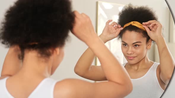 African american black woman styling curly afro hair. Makes hairstyle with hair band accessory