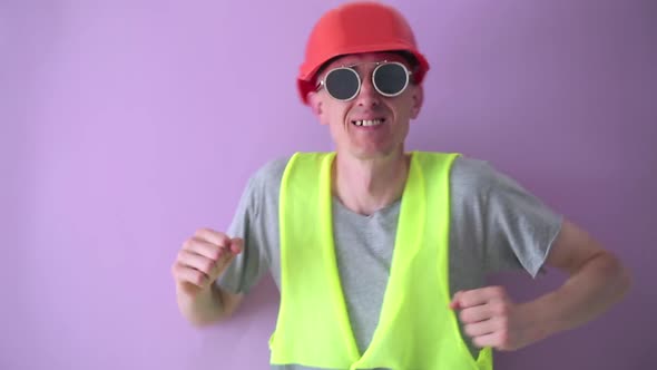 A man builder in a helmet dances moving rhythmically to the music.