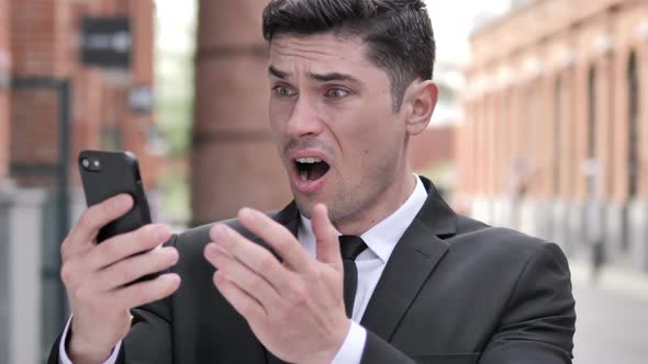 Outdoor Businessman Reacting to Loss Using Smartphone