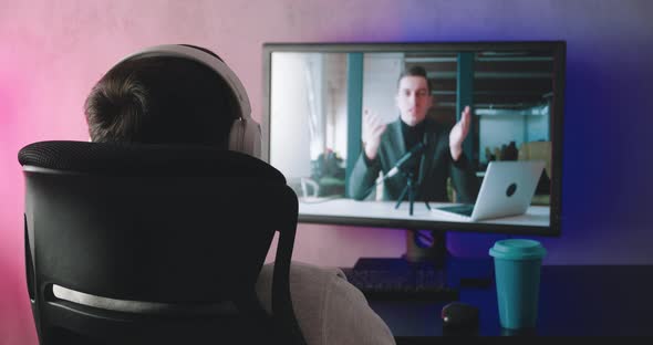 Rear View of a Young Man with Headphones Watching a Video Blog Indoors