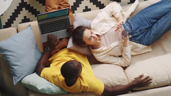 Diverse Couple Using Laptop and Smartphone on Sofa