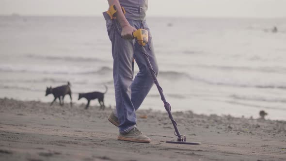 Unrecognizable Man with Electronic Metal Detector Scanning Sand on the Beach with Metal Detector