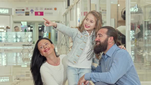 Cute Little Girl Pointing at the Clothing Store at the Mall, Shopping with Her Parents